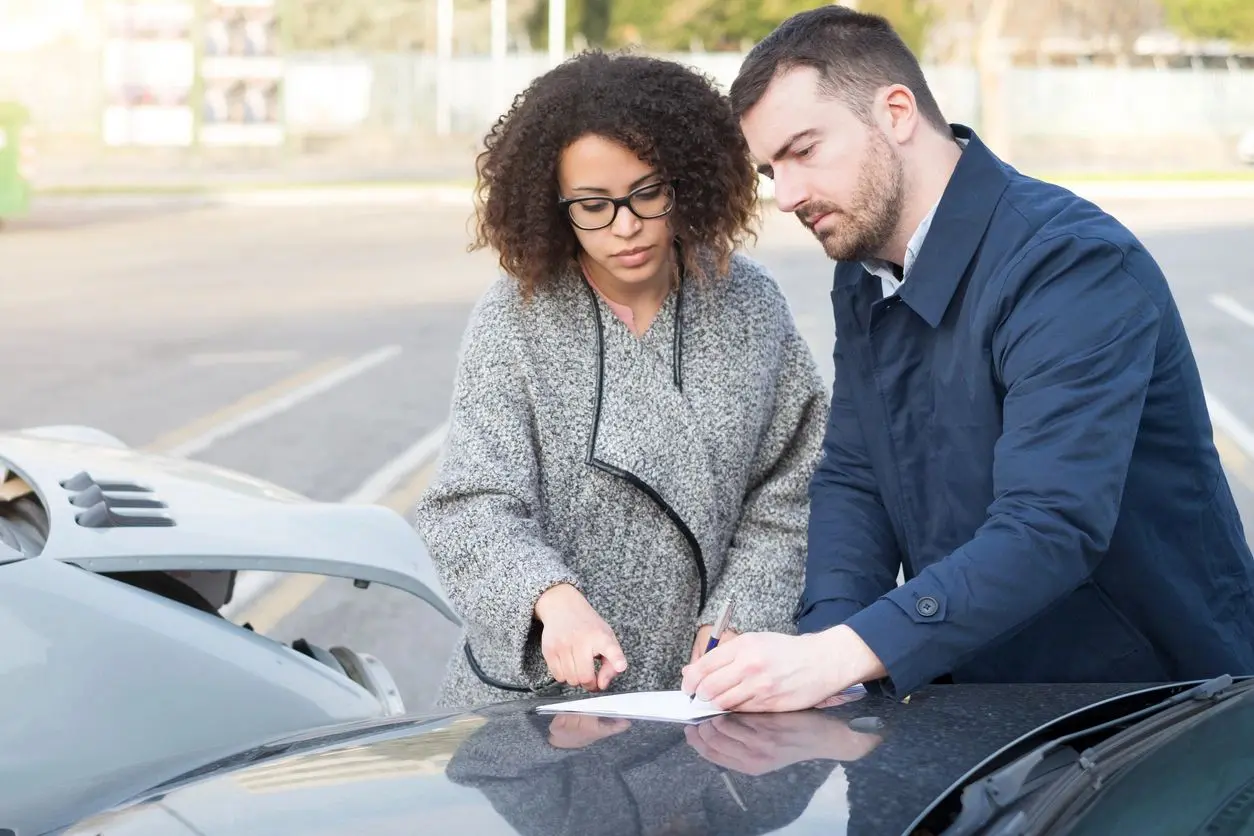 A woman and man signing papers on the hood of their car.